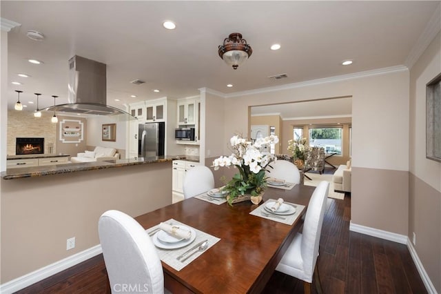 dining area featuring crown molding, a large fireplace, and dark hardwood / wood-style floors