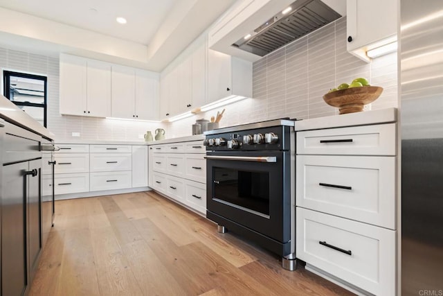 kitchen featuring light hardwood / wood-style flooring, white cabinetry, high quality range, tasteful backsplash, and wall chimney exhaust hood