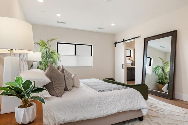 bedroom featuring a barn door, hardwood / wood-style floors, and multiple windows