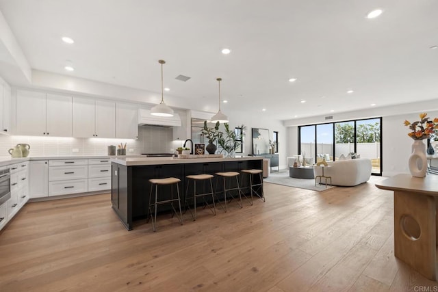 kitchen with a kitchen bar, tasteful backsplash, decorative light fixtures, an island with sink, and white cabinets