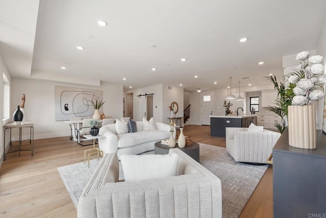 living room with a barn door, sink, and light wood-type flooring