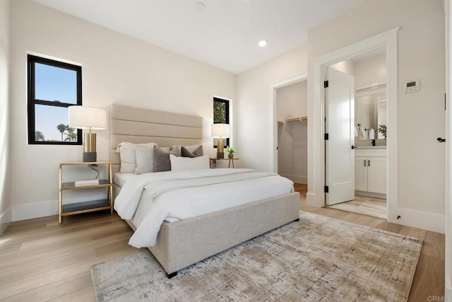 bedroom with a closet, a walk in closet, light hardwood / wood-style floors, and ensuite bath