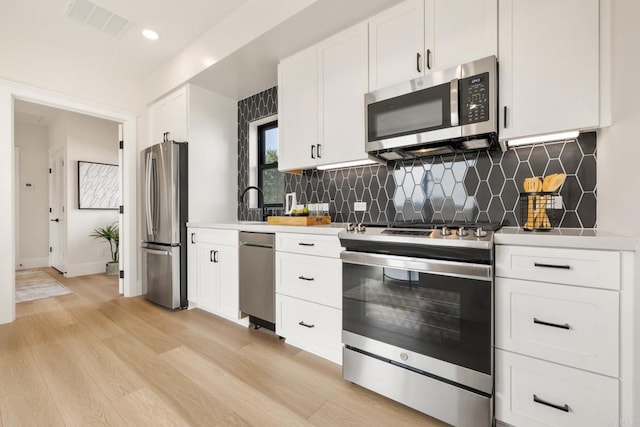 kitchen with tasteful backsplash, white cabinetry, appliances with stainless steel finishes, and light wood-type flooring