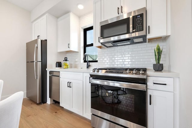 kitchen featuring appliances with stainless steel finishes, sink, white cabinets, decorative backsplash, and light hardwood / wood-style floors