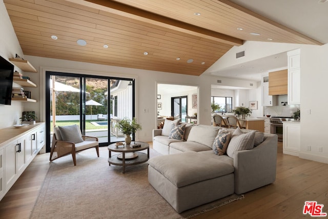 living room featuring vaulted ceiling with beams, a wealth of natural light, and light hardwood / wood-style flooring