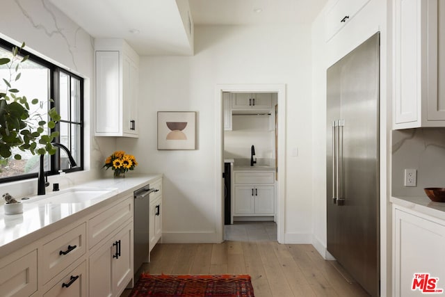 kitchen featuring white cabinetry, stainless steel appliances, sink, and light hardwood / wood-style flooring