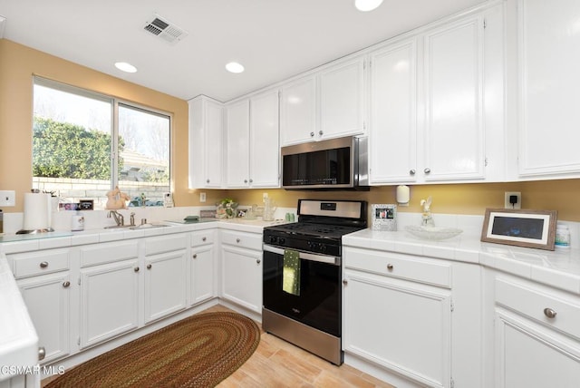 kitchen with sink, white cabinetry, tile countertops, light wood-type flooring, and stainless steel appliances