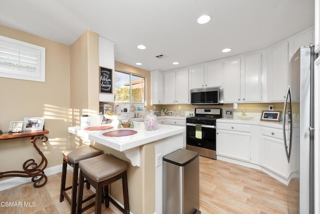 kitchen featuring tile counters, a breakfast bar area, white cabinets, and appliances with stainless steel finishes