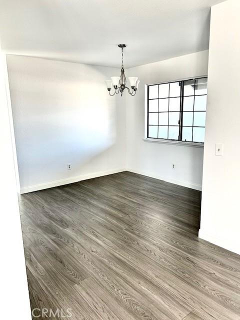 spare room with an inviting chandelier and dark wood-type flooring