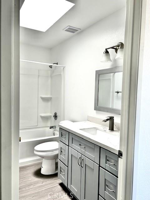 full bathroom with toilet, a skylight, shower / bathing tub combination, vanity, and hardwood / wood-style floors