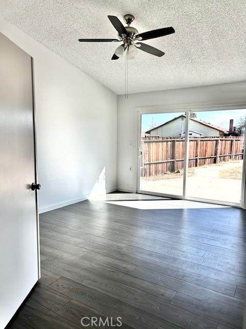 empty room featuring ceiling fan, dark wood-type flooring, and a textured ceiling