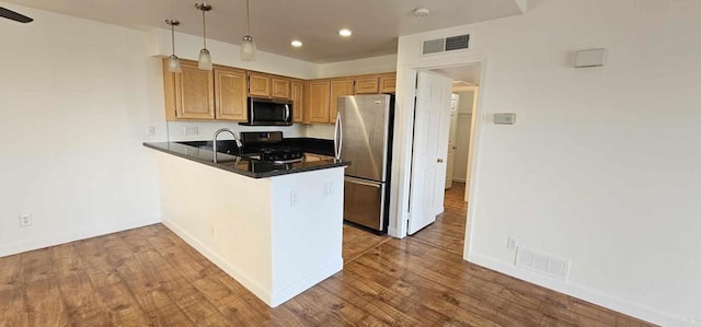 kitchen with appliances with stainless steel finishes, hardwood / wood-style floors, decorative light fixtures, sink, and kitchen peninsula