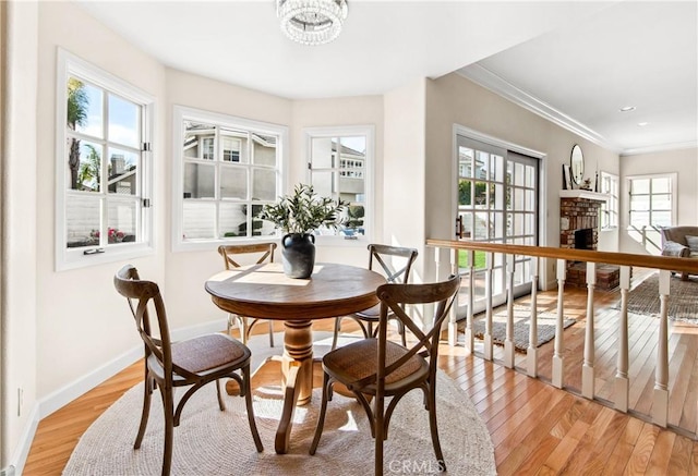 dining space with a fireplace, baseboards, light wood finished floors, an inviting chandelier, and crown molding