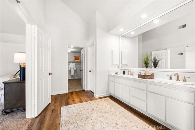 full bathroom featuring double vanity, visible vents, a spacious closet, a sink, and wood finished floors