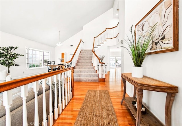 corridor with stairs, high vaulted ceiling, and wood finished floors