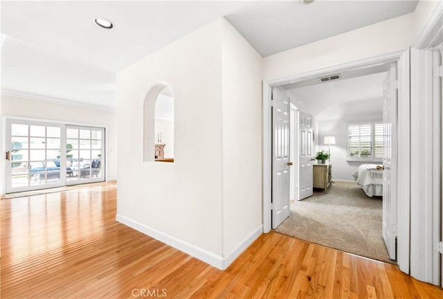 hallway with light wood-type flooring, baseboards, visible vents, and arched walkways