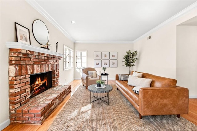 living room featuring crown molding, visible vents, a brick fireplace, wood finished floors, and baseboards