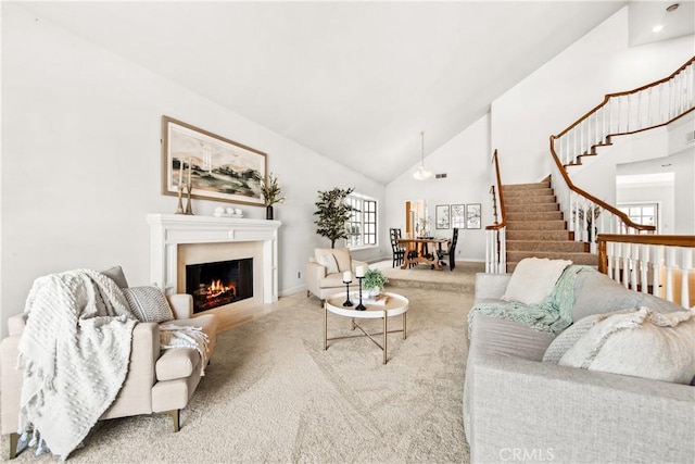 living room with baseboards, light colored carpet, a lit fireplace, stairs, and high vaulted ceiling