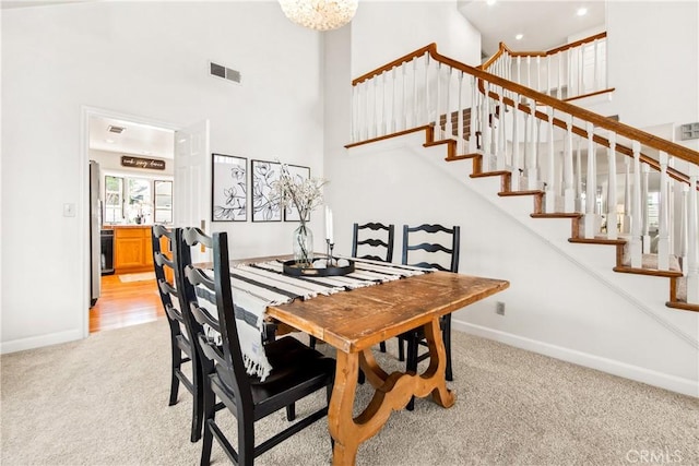 dining area featuring baseboards, a towering ceiling, visible vents, and light colored carpet