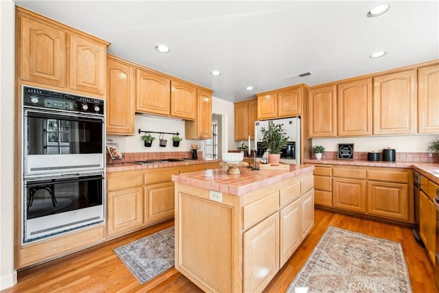 kitchen with tile countertops, double oven, gas stovetop, refrigerator with ice dispenser, and light wood-type flooring