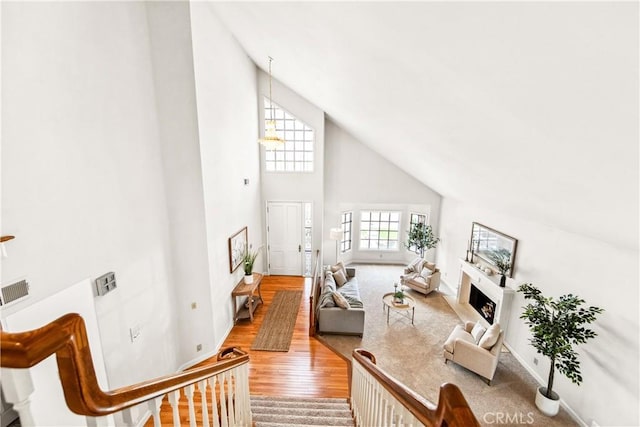 living room with baseboards, visible vents, light wood-style flooring, a fireplace, and high vaulted ceiling