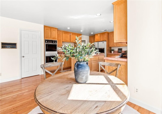 kitchen with tile countertops, recessed lighting, dobule oven black, light wood finished floors, and stainless steel fridge