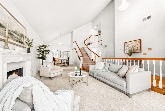 living room featuring a warm lit fireplace, high vaulted ceiling, stairs, and visible vents