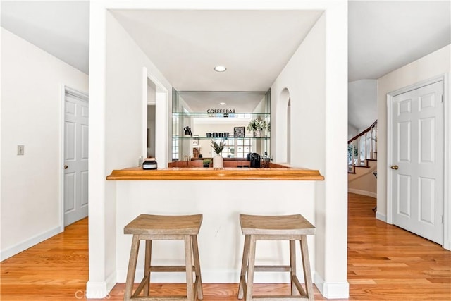 bar featuring stairs, baseboards, light wood-style flooring, and wet bar