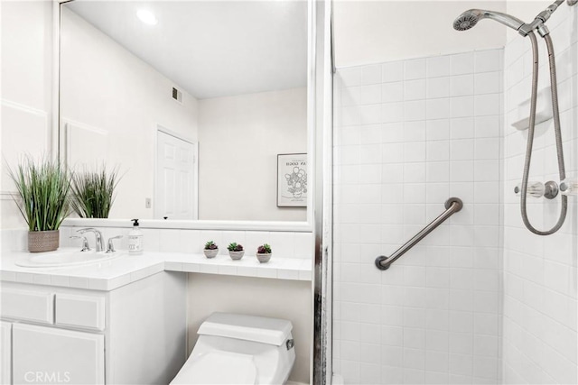 bathroom with toilet, visible vents, a tile shower, and vanity