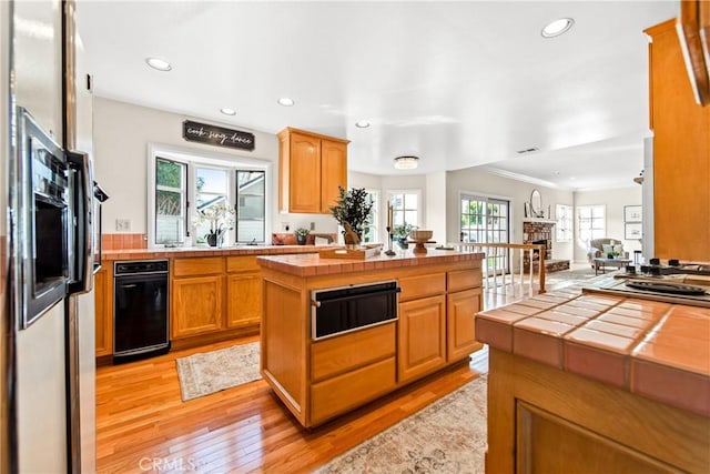 kitchen featuring a warming drawer, light wood finished floors, tile counters, and a healthy amount of sunlight