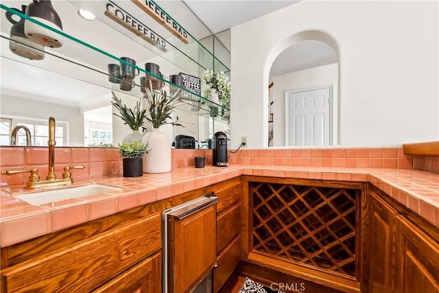 bar with crown molding, arched walkways, and a sink