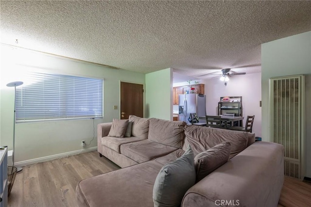 living area with baseboards, a heating unit, a ceiling fan, a textured ceiling, and light wood-style floors