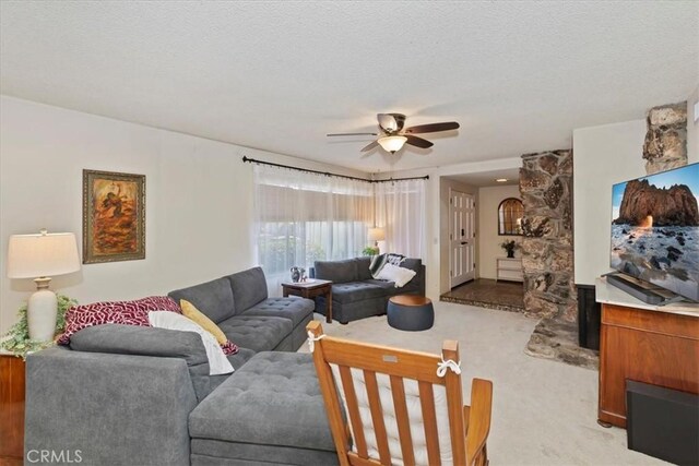 carpeted living room featuring a stone fireplace, a textured ceiling, and ceiling fan