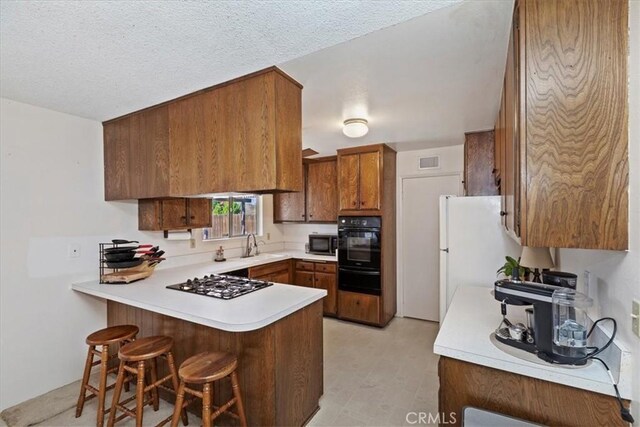 kitchen with a breakfast bar, kitchen peninsula, a textured ceiling, and black appliances