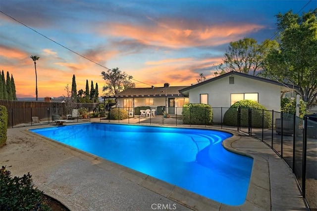 pool at dusk featuring a diving board and a patio area