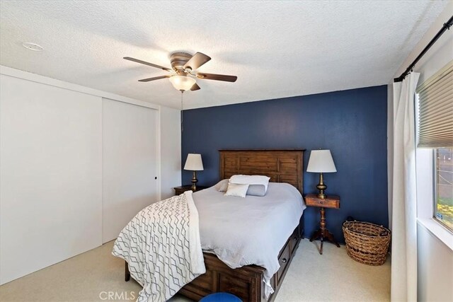 bedroom with ceiling fan, a closet, a textured ceiling, and carpet flooring