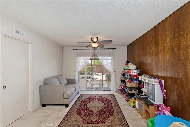 playroom with light carpet, ceiling fan, a textured ceiling, and wood walls