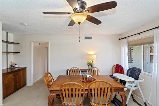 dining space featuring light carpet, ceiling fan, and a textured ceiling