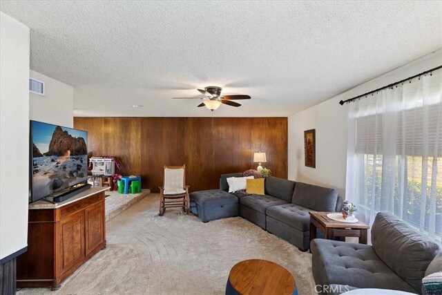 carpeted living room with ceiling fan, a textured ceiling, and wood walls