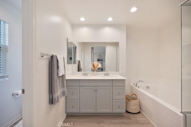 bathroom featuring vanity, tiled tub, and wood-type flooring