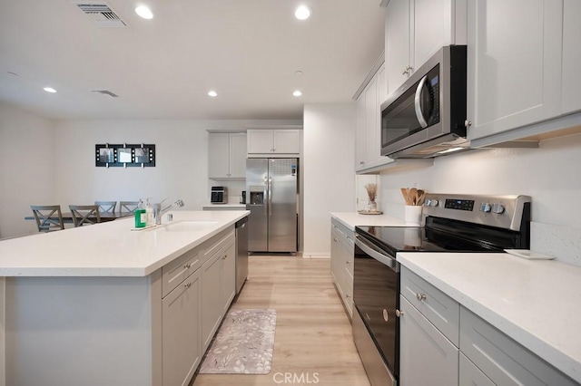 kitchen featuring appliances with stainless steel finishes, white cabinetry, sink, a kitchen island with sink, and light wood-type flooring