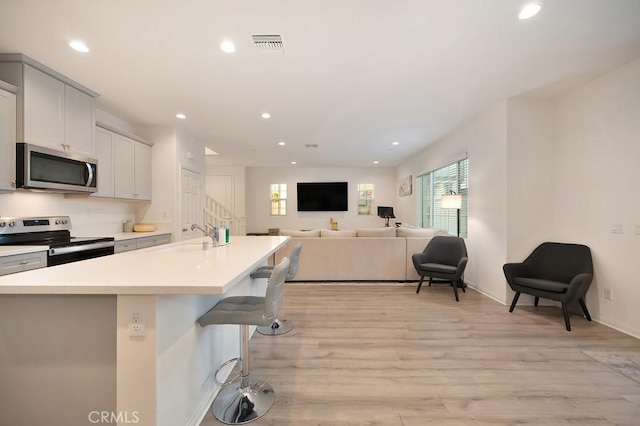 kitchen featuring sink, a breakfast bar area, appliances with stainless steel finishes, a kitchen island with sink, and light wood-type flooring