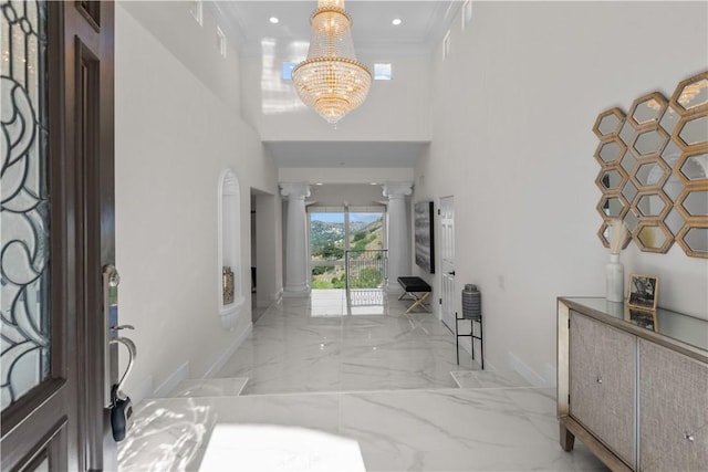 foyer with decorative columns, ornamental molding, a high ceiling, and an inviting chandelier