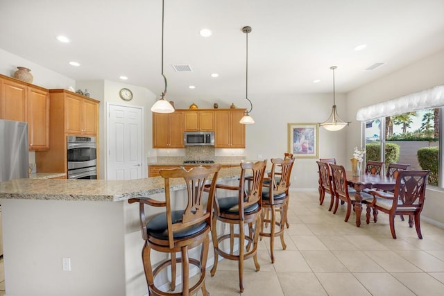 kitchen featuring light tile patterned floors, a breakfast bar, appliances with stainless steel finishes, backsplash, and decorative light fixtures