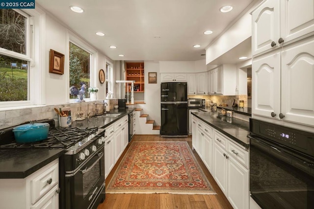 kitchen with sink, hardwood / wood-style floors, tasteful backsplash, black appliances, and white cabinets