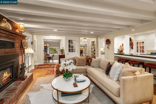 living room with a brick fireplace, beam ceiling, and light hardwood / wood-style floors