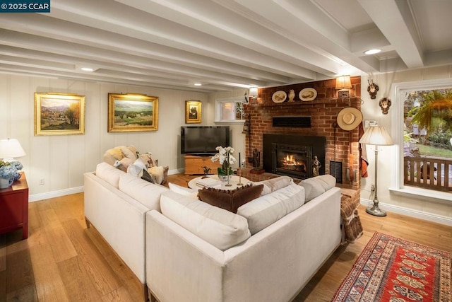 living room featuring beam ceiling, light hardwood / wood-style floors, and a brick fireplace