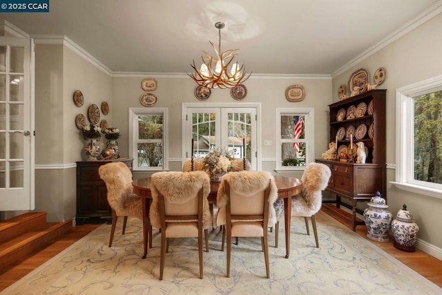 dining area featuring an inviting chandelier, light hardwood / wood-style flooring, ornamental molding, and french doors