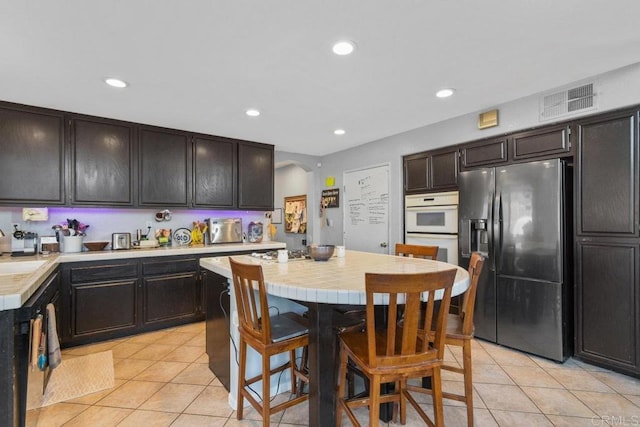 kitchen featuring sink, light tile patterned floors, stainless steel refrigerator with ice dispenser, white oven, and dark brown cabinets