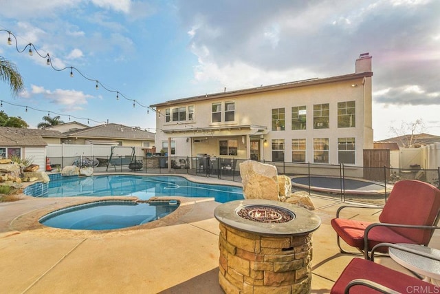 back of property with a swimming pool with hot tub, a patio area, and a fire pit